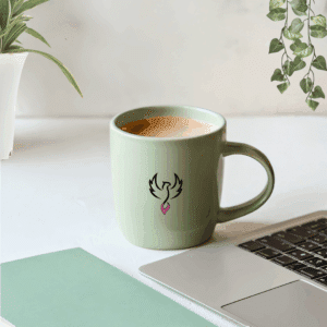 Schreibtisch mit grünem Häferl, Laptop, grünem Notizbuch, 2 Pflanzen