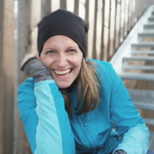 Rosa lachend, türkise Wanderjacke und schwarze Mütze