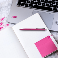 Laptop. Notizbuch. Post-It, Büroklammern und Kugelschreiber in pink